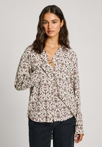 Camicia a maniche lunghe con motivo floreale in tonalità di blu, rosso e verde su sfondo crema. Presenta un colletto a punta e polsini con bottoni.