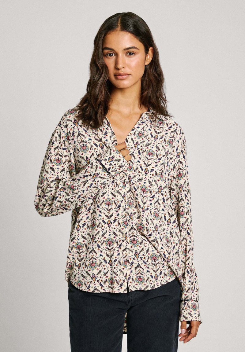 Camicia a maniche lunghe con motivo floreale in tonalità di blu, rosso e verde su sfondo crema. Presenta un colletto a punta e polsini con bottoni.