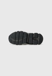 Semelle de chaussure en caoutchouc noir avec des profondeurs et des motifs variés, présentant une section centrale lisse et des accents surélevés pour la traction.