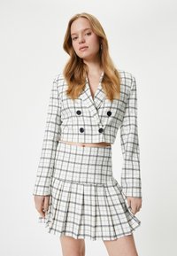 Weißes karierter, kurz geschnittenes Blazer mit schwarzen Linien, doppelreiher Design, kombiniert mit einem passenden gefalteten Minirock, elegant und schmal geschnitten.