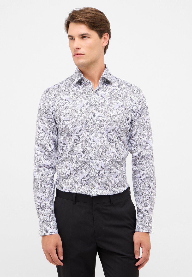 Witte langemouwenshirt met zwart ingewikkeld paisley ontwerp, met een spitse kraag en knoopsluiting, gecombineerd met zwarte broek.