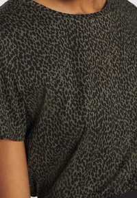 Krátký rukáv v tmavozelené látce s černým zvířecím vzorem. Má kulatý výstřih a měkký, strukturovaný materiál.