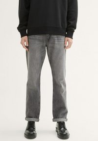 Szare dżinsy z luźnym krojem, z podwiniętymi nogawkami i delikatnym przetarciem. W połączeniu z czarnymi butami i czarną bluzką z długim rękawem.