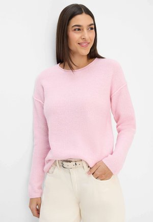 Hellrosa gestrickter Pullover mit Rundhalsausschnitt, überschnittenen Schultern und gerippten Bündchen, kombiniert mit cremefarbener Hose und einem Gürtel.