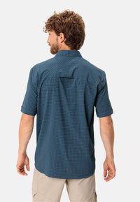 Camisa de manga corta en azul oscuro con un patrón de cuadros, que presenta un cuello tradicional, mangas enrolladas y un detalle de yugo en la parte posterior.