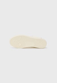 Sneaker sole made of rubber, featuring a textured pattern for traction, in off-white color with a subtle logo detail near the heel.