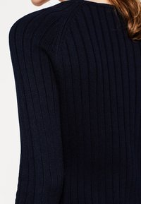 Pull en tricot bleu marine avec texture à côtes verticales, présentant un col rond et des manches longues, mettant en valeur une silhouette ajustée.