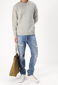 Ljusgrå stickad tröja, blå slitna jeans och vita sneakers. Ytterligare detalj: tan tygväska med minimal design.