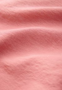 Tissu rose doux avec des plis subtils et une surface lisse légèrement texturée.