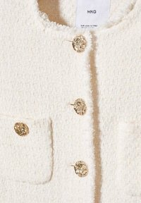 Veste en maille à texture crème avec quatre boutons dorés ornés et deux poches à l'avant, étiquetée MNG, taille EUR-USA S/MEX.