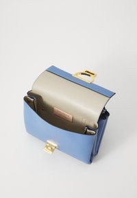 Uformowana torebka wykonana z jasno niebieskiej skóry z fakturą, z beżowym wnętrzem, złotymi akcentami i charakterystycznym zapięciem.