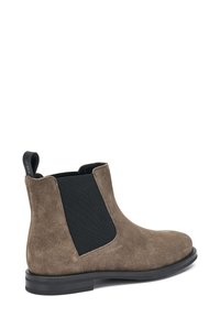 Botas Chelsea de ante marrón con paneles laterales elásticos negros, puntera redondeada y tirador en la parte posterior. Suela plana de goma.