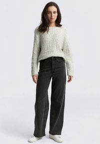 Pletený svetlosivý sveter s textúrovaným vzorom, doplnený o čierne džínsy s vysokým pásom a širokými nohavicami a biele tenisky.