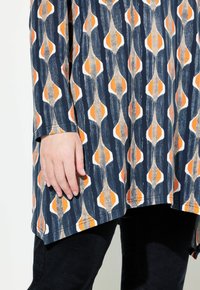 Marineblaues Tunika mit einem abstrakten Muster aus orangen, weißen und beigen Elementen. Lange Ärmel, abgerundeter Saum und weiche Stofftextur.