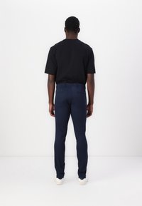 Marinblå slim-fit byxor med en slät textur och två bakfickor, tillsammans med en enfärgad svart t-shirt med kort ärm och vita sneakers.