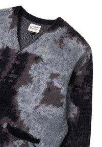 Cardigan abbottonato con texture morbida, motivo astratto in bianco e nero, scollo a V e una piccola tasca frontale sul lato inferiore.