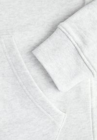 Felpa grigio chiaro caratterizzata da una texture morbida, tasca a marsupio e maniche con polsini. I dettagli delle cuciture sono visibili.