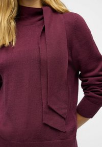 Bordeaux sweater med funnel neck og lange, hængende bånd detaljer. Strikket tekstur med ribbede manchetter og kant. Blødt, let stof.