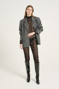 Blazer gris de gran tamaño sobre un bodysuit de encaje negro, combinado con botas de rodilla negras y brillantes. El blazer tiene solapas de muesca y bolsillos de parche.