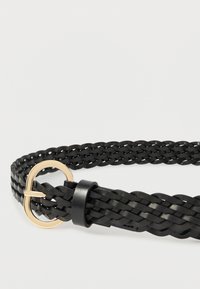 Cintura in pelle intrecciata nera con una piccola fibbia rettangolare dorata e un anello in pelle nera su uno sfondo bianco.