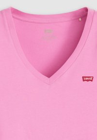 Rožinė v-kaklo marškinėlių suknelė pagaminta iš medvilnės, su lygiu paviršiumi. Kairėje krūtinės pusėje yra raudonas Levi's logotipas. Paprastas ir kasdieniškas dizainas.