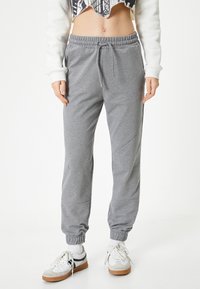 Grijze sportbroek met een elastische tailleband en enkelboorden. Bevat zijnaad en heeft een ontspannen pasvorm, gecombineerd met witte sportschoenen.