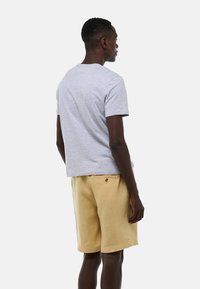 T-shirt en coton gris à manches courtes, associée à un short en lin beige avec une poche au dos et un détail de bouton.