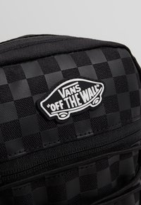 Schwarzer Schachbrett-Rucksack aus strukturiertem Material mit Gummi-Vans-Logo-Patch. Verfügt über Reißverschlüsse und stabile Nähte entlang der Kanten.