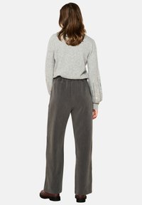 Gray knitted sweater with balloon sleeves and silver sequin accents, paired with loose-fitting, textured dark gray trousers.
