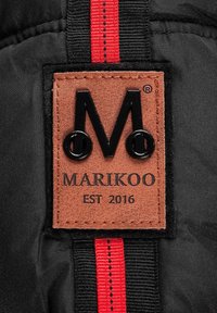 Black fabric with a brown leather label featuring black embossed letters "M" and "MARIKOO EST 2016," and a red accent ribbon.