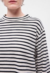 Sweater riscado com um decote alto, feito de um tecido macio. O design alterna entre riscas horizontais em creme e azul-marinho.