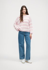 Pulôver de malha às riscas rosa claro e branco com um corte descontraído, combinado com jeans azuis largos e ténis brancos.