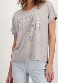 Camiseta corta de manga en gris claro con un diseño de texto reflectante que incluye frases como "QUIérete A TI MISMO." Tela suave, ajuste relajado, estilo casual.