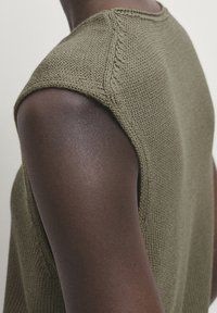 Khaki knitted sleeveless top featuring a textured fabric, crew neckline, and intricate stitching along the shoulder seams.