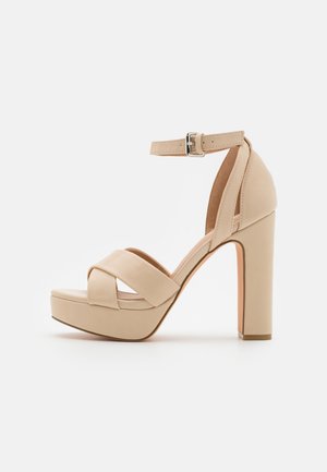 Beige platform sandals with a high heel and ankle strap. Made of smooth material with crossed front straps. Flat sole base.