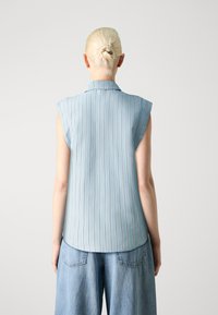 Blusa senza maniche azzurro chiaro con colletto e righe verticali. Tessuto morbido con una texture liscia, orlo arrotondato e vestibilità rilassata.