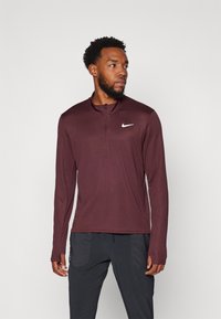 Bordo majica dugih rukava za sport s četvrtastim patentnim zatvaračem i bijelim Nike logotipom na lijevoj strani prsnog koša. Mekani, rastezljivi materijal s prilagođenim dizajnom.