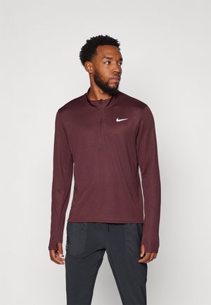 Camiseta atlética de manga larga en color burdeos con cremallera de un cuarto y un logo de Nike en blanco en el lado izquierdo del pecho. Tejido suave y elástico con un diseño ajustado.