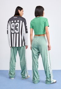 Camisa de mangas longas às riscas pretas e brancas com o número 93, combinada com uma camisa verde cropped e calças de treino verdes em satin com riscas laterais.