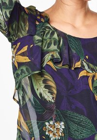 Blusa con stampa floreale caratterizzata da maniche a rouches, tessuto trasparente e colori vivaci come verde, giallo e viola, con distintivi motivi a foglia.