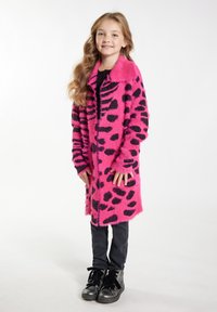 Ružičasti krzneni kaput s crnim leopard uzorcima, s ovratnikom, dugim rukavima i ravnim krojem. Uparen s crnim uskim hlačama i čizmama.