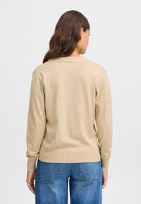 Pull en tricot beige avec des poignets et un ourlet côtelés, doté d'un col rond et de manches longues. Texture unie, porté avec un jean en denim bleu.