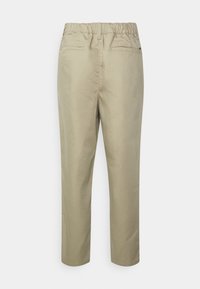 Pantaloni beigi a gamba affusolata con cintura elasticizzata e due tasche posteriori a soffietto, mostrati da dietro su uno sfondo bianco semplice.