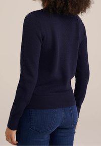 Marinblå strukturerad tröja med ribbad nederkant och ärmar, med en figurnära design, visad bakifrån mot en ljus bakgrund.