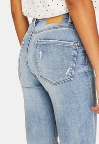 Ljusblå denimjeans med en fitted design, med slitningar, två bakfickor och en tan läderetikett vid midjan.