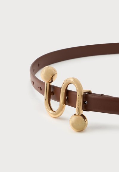 Ceinture en cuir marron avec une boucle dorée abstraite en forme de ligne courbe se terminant par deux boules rondes.