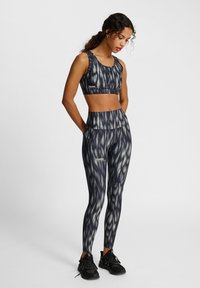 Zwart en grijs sportset bestaande uit een geknipt tanktop en hoogzit leggings met een gestructureerd, abstract patroon. Gestructureerde stof en discreet logo.