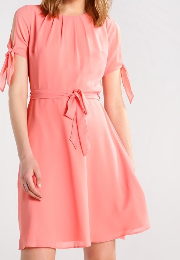 Kortärmad, korallfärgad klänning i lätt tyg med figursydd midja och knytningar på ärmarna. A-linjeformad med en fladdrande kjol.