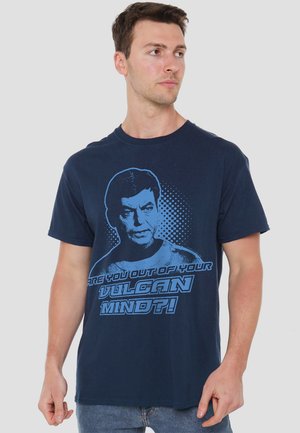 Navyblaue Baumwoll-T-Shirt mit einem grafischen Design eines Charakters, dessen Gesicht in Blau dargestellt ist, sowie dem Text "BIST DU AUS DEINEM VULKANISCHEN GEIST AUSGETRETEN?!"