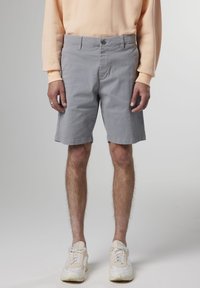 Shorts di cotone grigi con frontale piatto, chiusura con bottone e tasche laterali; indossati con una camicia a maniche lunghe pesca e sneakers bianche.